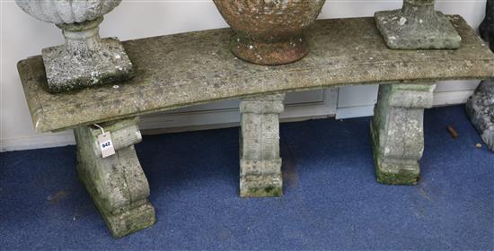 A weathered composition garden bench, of concave rectangular form, with three scroll plinths, 4ft 8in.